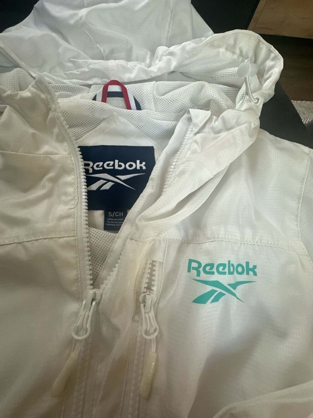Reebok Women's White Lightweight Hooded Windbreaker Jacket with Teal Spellout